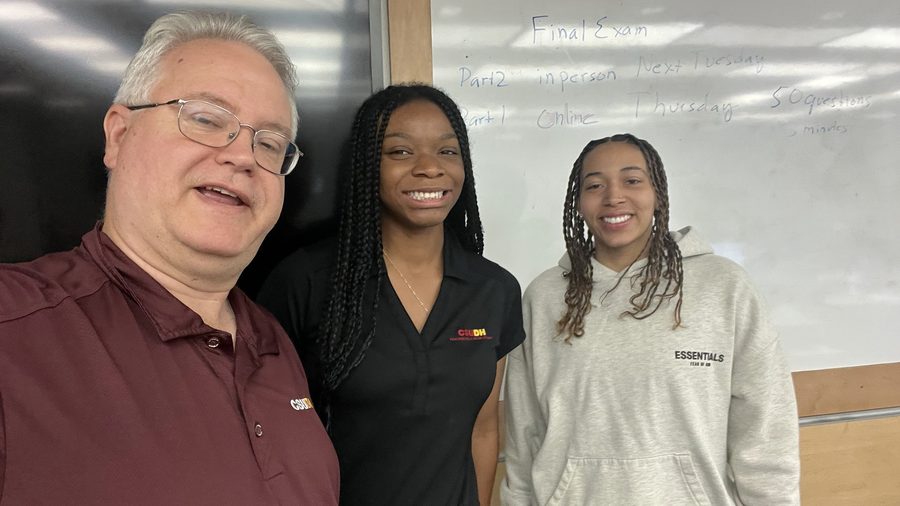 Thomas Norman with two students in front of a whiteboard listing final exam details
