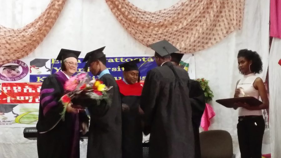 Thomas Norman in regalia receiving flowers on stage at a university graduation in Ethiopia